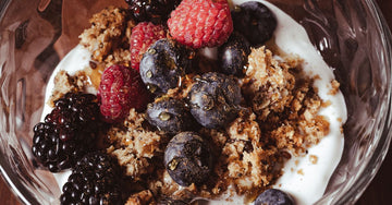Glass bowl of yogurt with fresh berries, granola and nuts on a wooden table