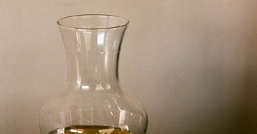 A glass pitcher and a glass of water on a wooden table in soft natural light