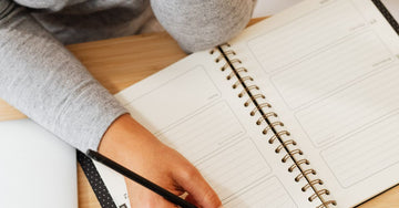 Overhead view of a person writing in a notebook at a desk, warm morning light