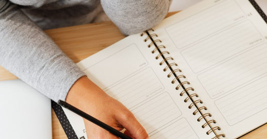 Overhead view of a person writing in a notebook at a desk, warm morning light
